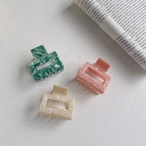 Three geometric acetate hair claws in green, pink, and cream with marble textures