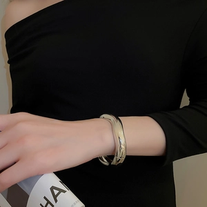 Detailed close-up of a silver wavy metal bangle with a polished mirror finish on a wrist