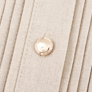 Detail shot of golden round metal buttons on off-white pleated linen fabric texture