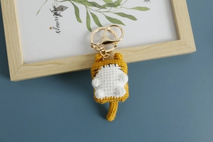 Close-up of handmade yellow and white crochet cat keychain with gold metal ring and clip