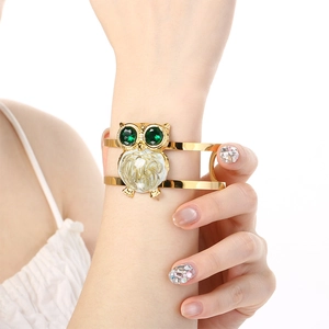 Detail of owl gold open cuff bracelet with green gems and white enamel on wrist