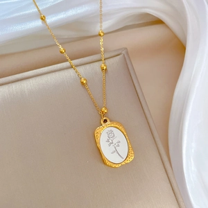 Close-up of golden rose pendant with white shell inlay and beaded chain on silk