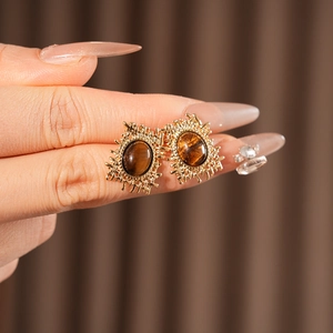Macro shot of gold square earrings with oval tiger eye stones worn by a model