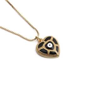 Détail du pendentif cœur doré avec œil en émail noir sur une chaîne à maillons