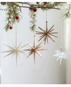 Detailed view of champagne and white star ornaments hanging on festive pine branches