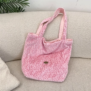 Détail d'un sac cabas en peluche léopard rose avec logo en métal sur canapé blanc
