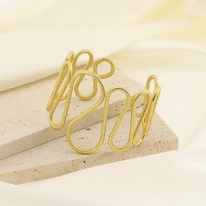 Detailed close-up of golden wavy open cuff bracelet on a stone tray with silk