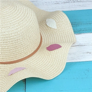 Detail of wide brim straw hat with leaf appliques and wavy edge on wooden background