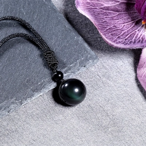 Pendentif sphérique en obsidienne 16mm avec cordon noir artisanal sur surface en pierre