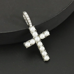 Close-up of a silver cross pendant with white pearls on a textured dark background