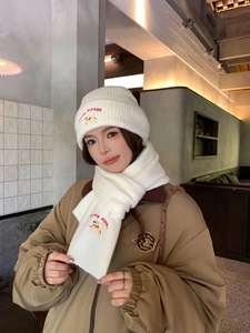 Close-up of white knit beanie and scarf set featuring dog embroidery and lucky lettering