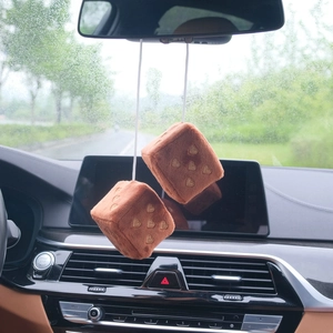 Close-up of brown plush dice car charms with gold hearts hanging on a rearview mirror