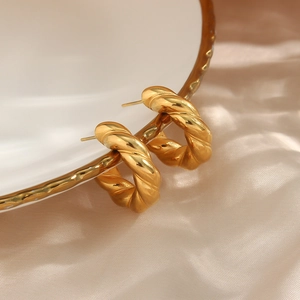 Close-up of gold twisted hoop earrings hanging on a white porcelain plate edge
