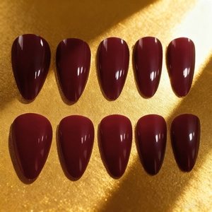 Lot de 10 faux ongles amande rouge foncé brillant sur une surface dorée texturée