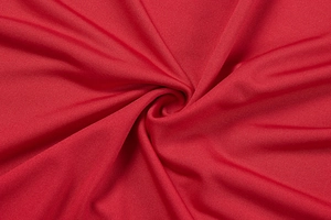 Macro view of red rib-knit fabric texture with elegant pleated swirl pattern