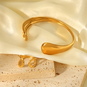 Detail view of gold teardrop open bangle and ring on stone pedestal with silk