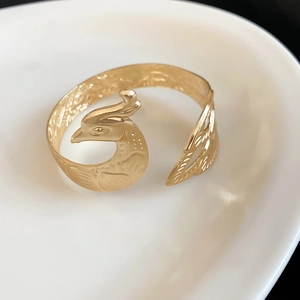 Elegantes goldenes Pfauen-Manschettenarmband mit Gravuren auf weißem Porzellangeschirr