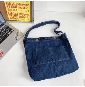 Detail view of a navy blue denim tote bag with square pockets on a white desk