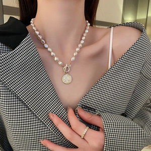 Detail view of pearl necklace with gold coin pendant and textured gold ring on model