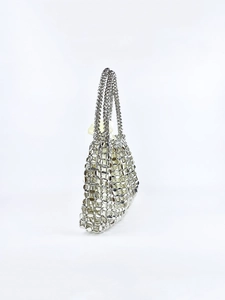 Detail of silver metallic hollow mesh handbag featuring shimmering sequins and woven chain handle