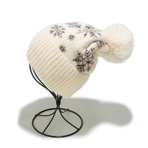Close-up of knit winter hat featuring snowflake patterns and large faux fur pompom detail