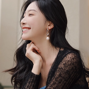 Fashionable golden hoop earrings with large white pearl drop worn by a smiling female model