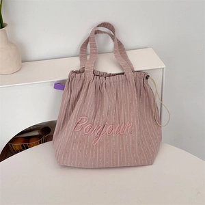 Detailed embroidery of Bonjour on a striped canvas tote bag with drawstring closure