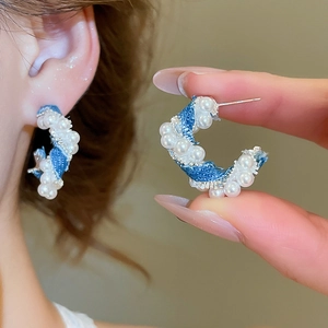 Close-up of C-shaped denim twist earrings with white pearls and silver needles