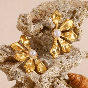 Detail of gold petal earrings with white pearls displayed on a textured natural rock