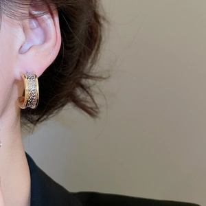 Close-up of two-tone C-shaped hoop earrings with hammered texture on female model