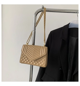 Close-up of beige quilted crossbody bag with gold chain strap on display stand