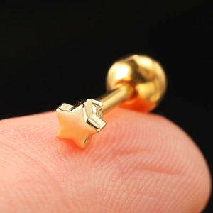 Macro shot of gold star piercing stud with screw back held on a fingertip for size reference