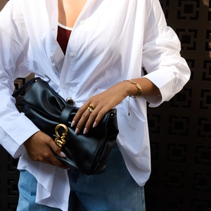 Close-up of black leather handbag with artistic gold metal clasp and matching jewelry