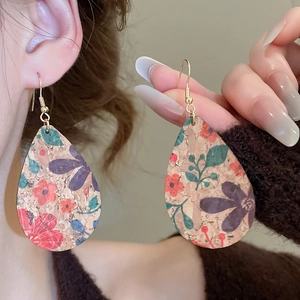 Close-up of teardrop leather earrings with vintage floral print and cork texture surface
