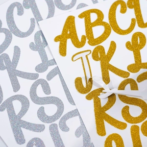 Close-up of gold glitter letter stickers with adhesive backing for DIY graduation caps