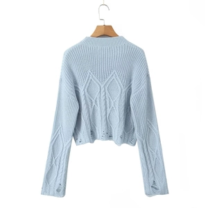 Detail of light blue cable knit sweater with distressed hem and ripped texture