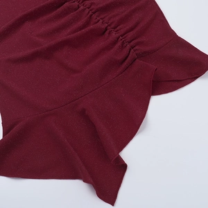 Dettaglio del vestito glitter rosso vino con bordi a balze e trama in maglia arricciata
