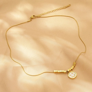Detail shot of golden necklace with square beads and white smiley face pendant on silk
