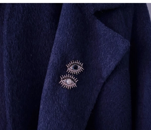 Detail of vintage evil eye brooches with blue gemstone and pearls on navy tweed coat