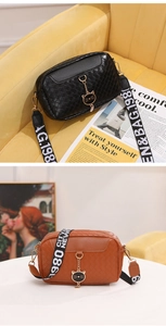 Detail showing woven leather texture and cat pendant on crossbody bag with wide strap
