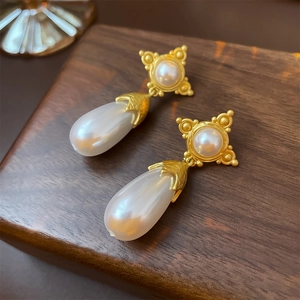 Détail des boucles d'oreilles vintage avec étoile dorée mate et perle en goutte