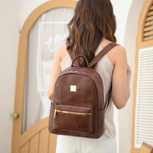 Detail of a brown leather backpack featuring a front zipper pocket and adjustable straps