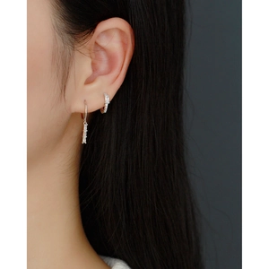 Detailed view of silver hoop earrings with rectangular zircon drops on a model's ear