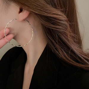 Detail view of large gold hoop earrings with faceted texture on elegant female model