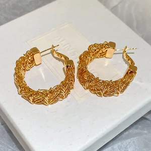 Close-up of gold-plated woven texture C-shape hoop earrings on white jewelry box
