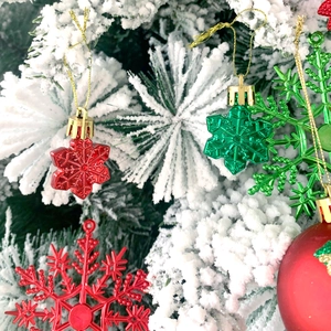 Dettaglio di fiocchi di neve rossi e verdi e pallina su rami di albero di Natale innevati