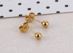 Macro shot of minimalist gold beaded heart earrings set on a textured pink background