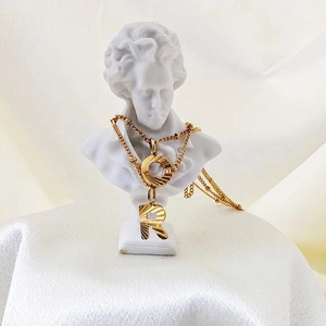 Detail of gold letter R pendant necklace on a white bust statue with elegant draping