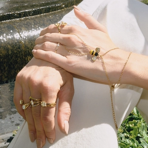Detail einer goldenen Bienen-Handkette und Lagenringen mit Zirkon-Details im Freien