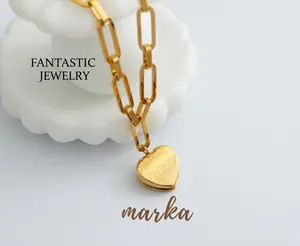 Macro detail of gold paperclip chain necklace with engraved heart pendant on white ceramic